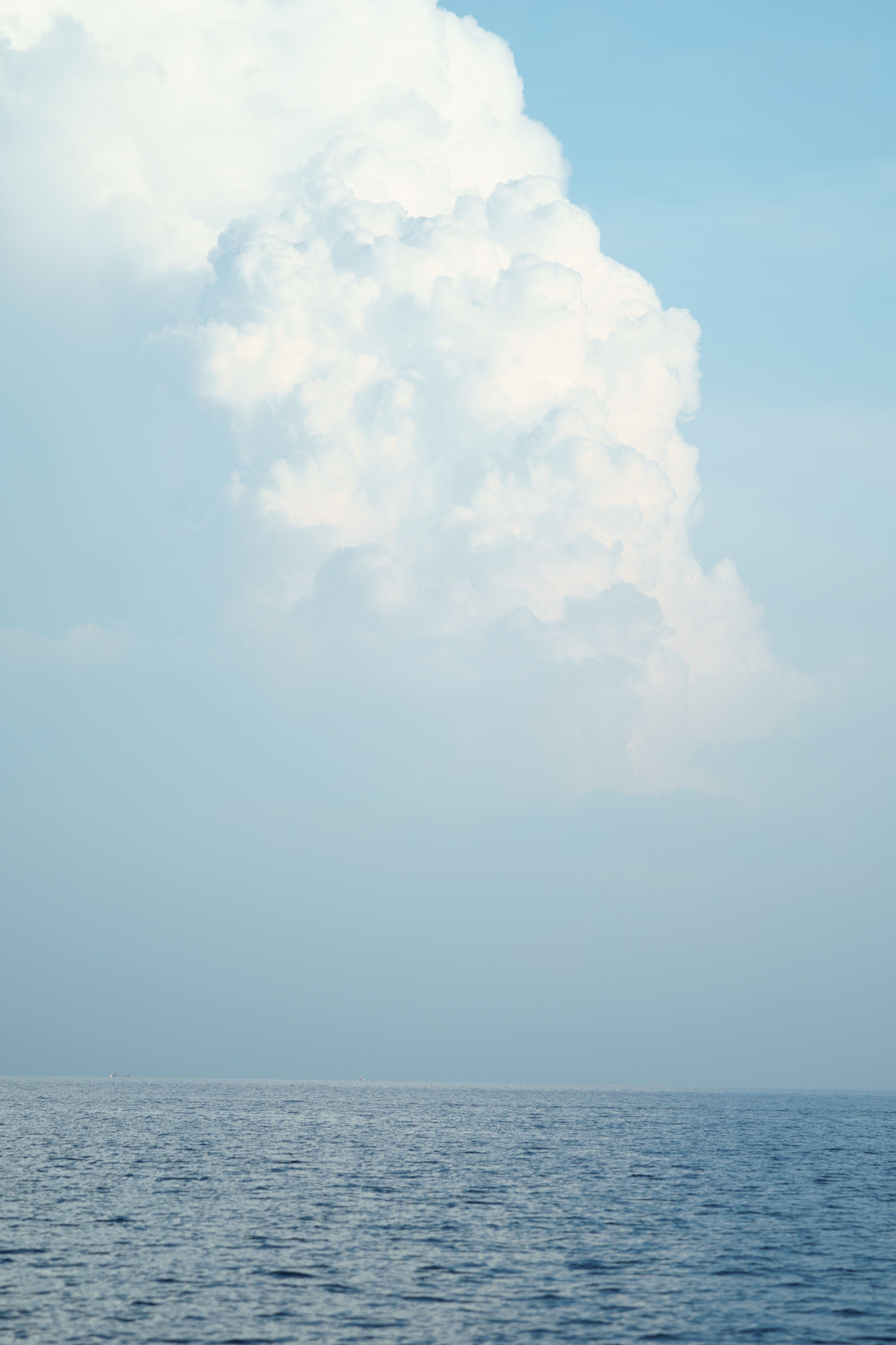 Serene ocean view with a towering cumulus cloud set against a clear blue sky.