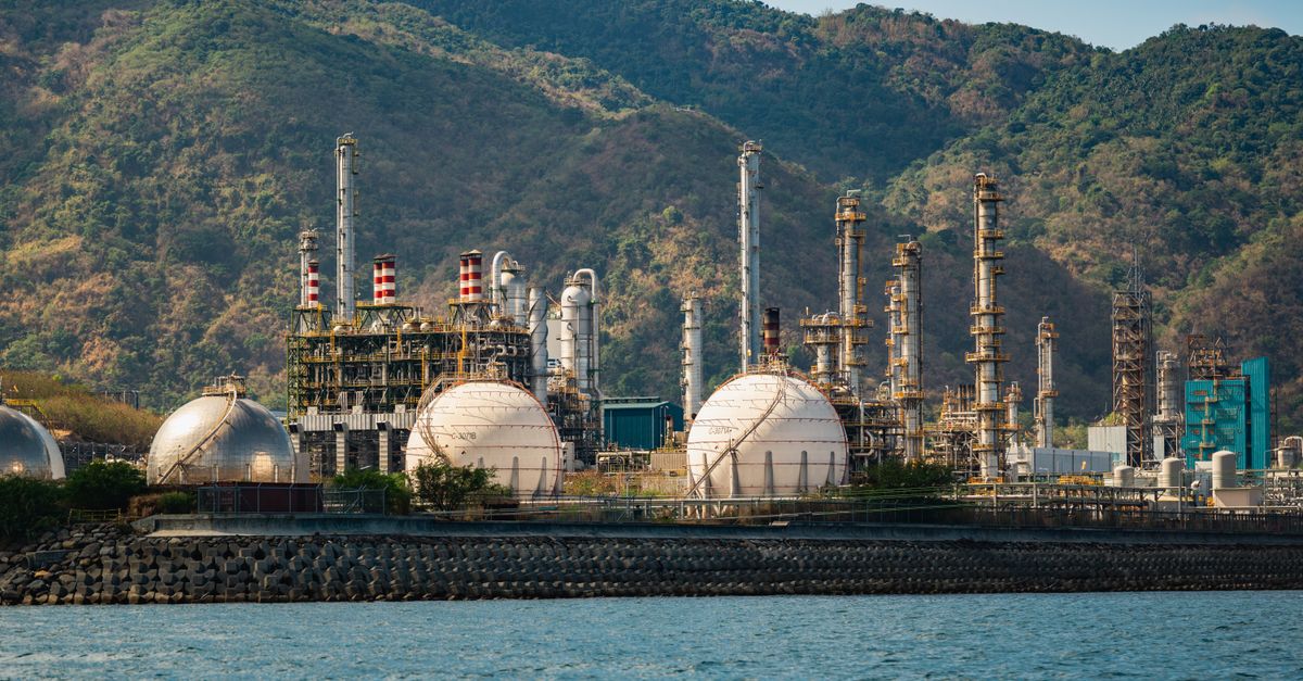 Industrial refinery with spherical tanks by the coastline against a backdrop of mountains.