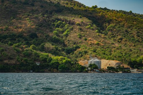 Free Lush green hills surrounding industrial silos by the coastal water under clear skies. Stock Photo