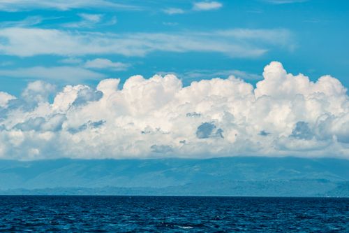 Free Majestic clouds over a serene ocean with distant mountains under a clear blue sky. Stock Photo