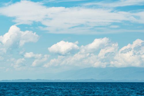 Free A tranquil ocean view with a vivid blue sky and fluffy white clouds. Stock Photo