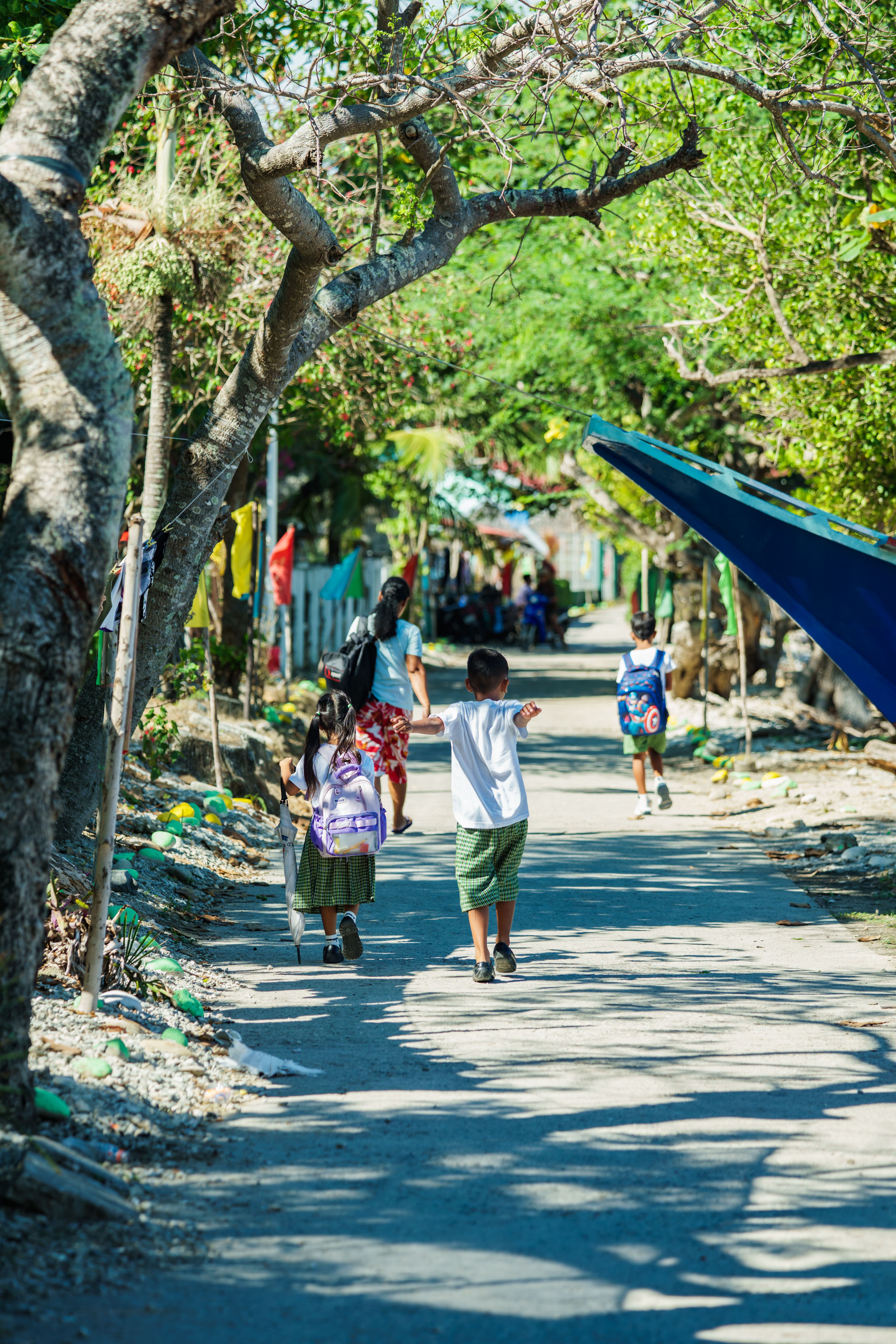 Group of children walking home from school on a scenic, sunlit pathway with lush greenery and trees.