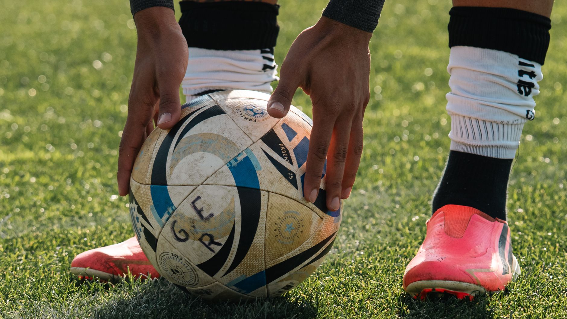 Close-up of football boots controlling a pass on artificial turf, cones and teammates blurred behind