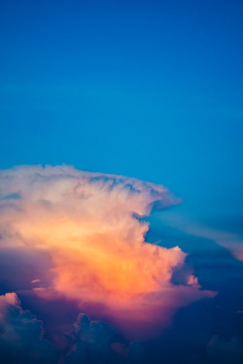 Free Dramatic cumulus cloud formation during sunset, casting vibrant colors against the clear blue sky. Stock Photo