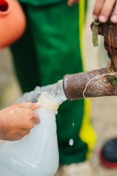 Close-up of a child collecting water from a rustic outdoor tap using a plastic container.