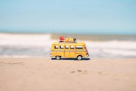 一辆充满活力的黄色玩具车停在以海洋为背景的沙滩上，象征着有趣的旅行冒险