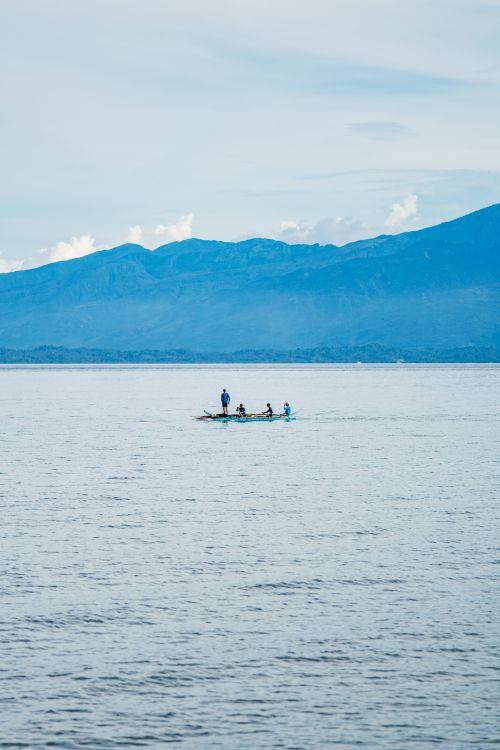 Free Three people enjoy boating on a calm lake with majestic mountains in the background on a clear day. Stock Photo