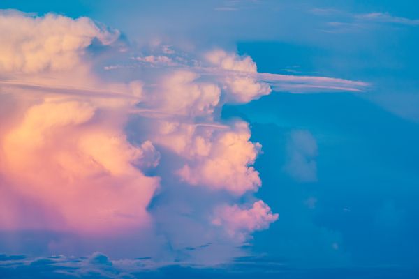 Vista impressionante de nuvens cúmulus parecidas com algodão doce em tons de rosa e azul durante o pôr do sol.