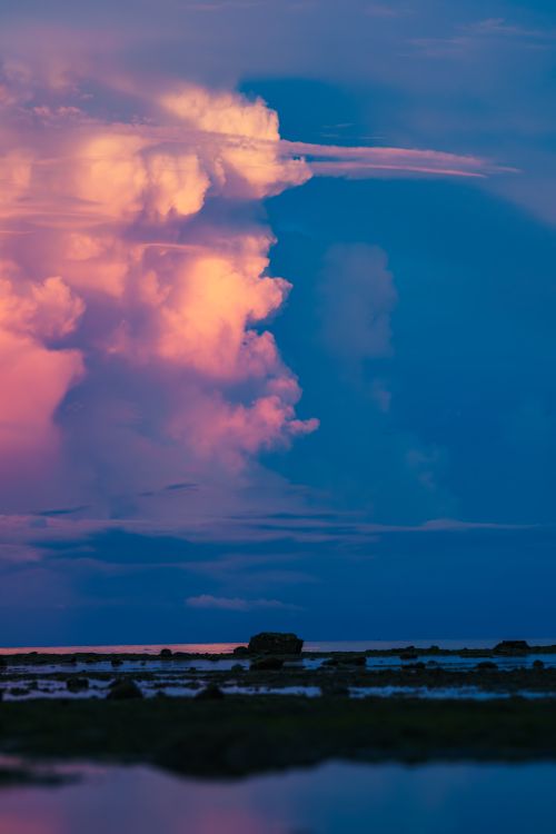 Free Vibrant, dramatic sunset clouds above an ocean horizon with reflections on the water. Stock Photo