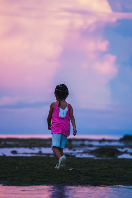Free A child walks on a beach at sunset, under vibrant pink and blue skies, creating a serene and dreamlike moment. Stock Photo