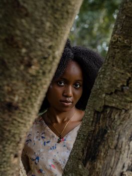 Portrait of a woman in nature framed by two tree trunks, creating a serene, natural setting.