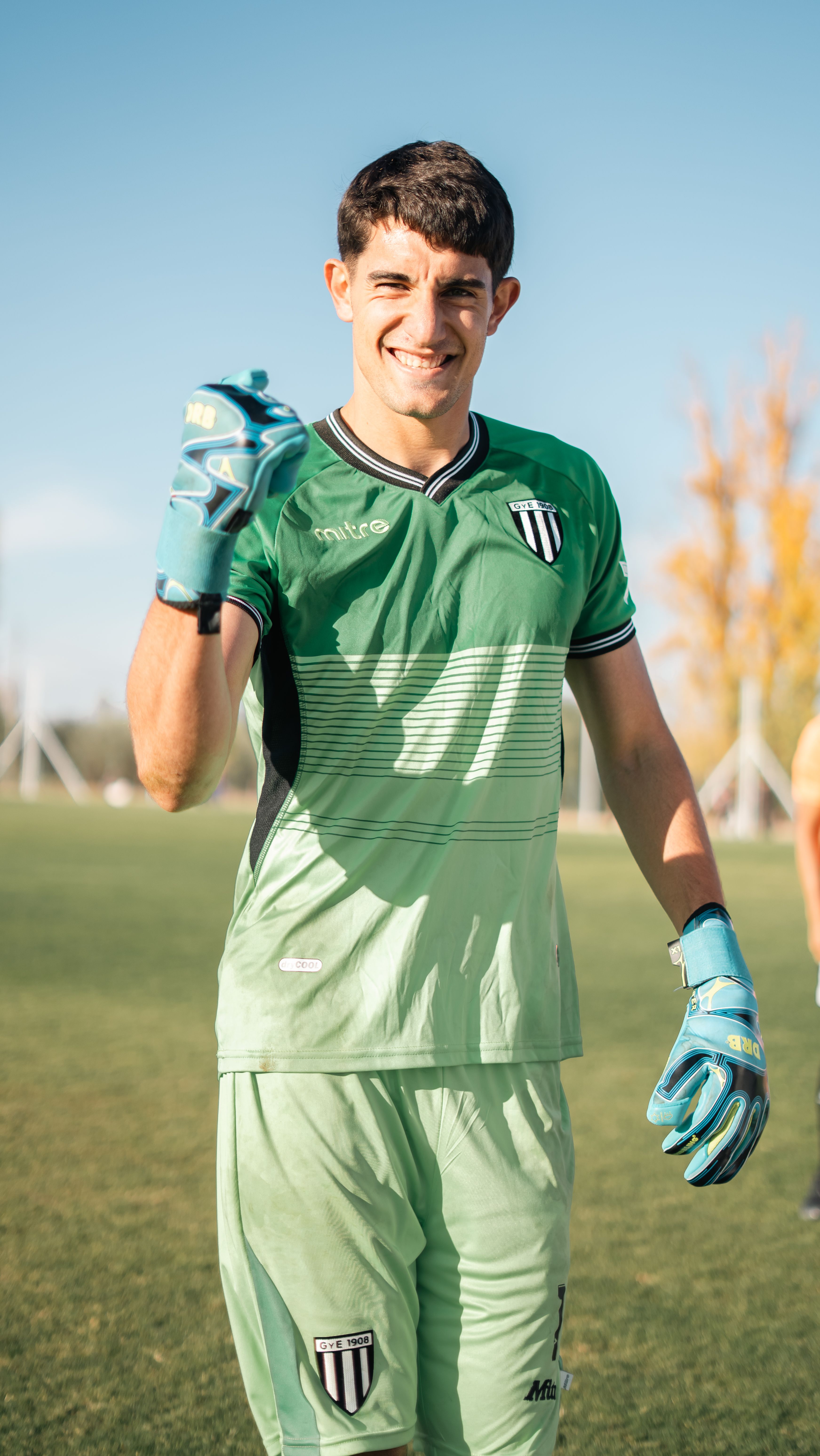 A soccer goalkeeper in green uniform celebrating on a sunny day outdoors.