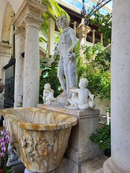 Elegant marble statue with children in a lush garden setting.