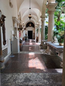 Mediterranean style arched hallway with stone columns and potted plants in a historical building.