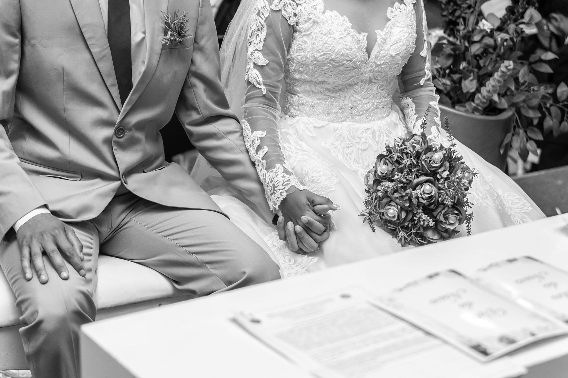 A newlywed couple's hands intertwined during their wedding ceremony, captured in black and white.