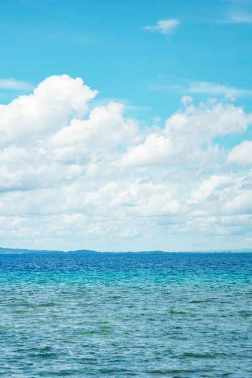 Free Peaceful ocean view with vibrant blue water and fluffy white clouds in the sky. Stock Photo