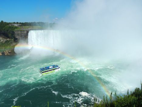 A stunning view of Niagara Falls with a rainbow and a boat navigating the waters.