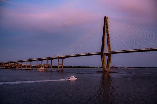 Free Scenic view of Charleston's Arthur Ravenel Jr. Bridge at sunset with a boat on the water. Stock Photo