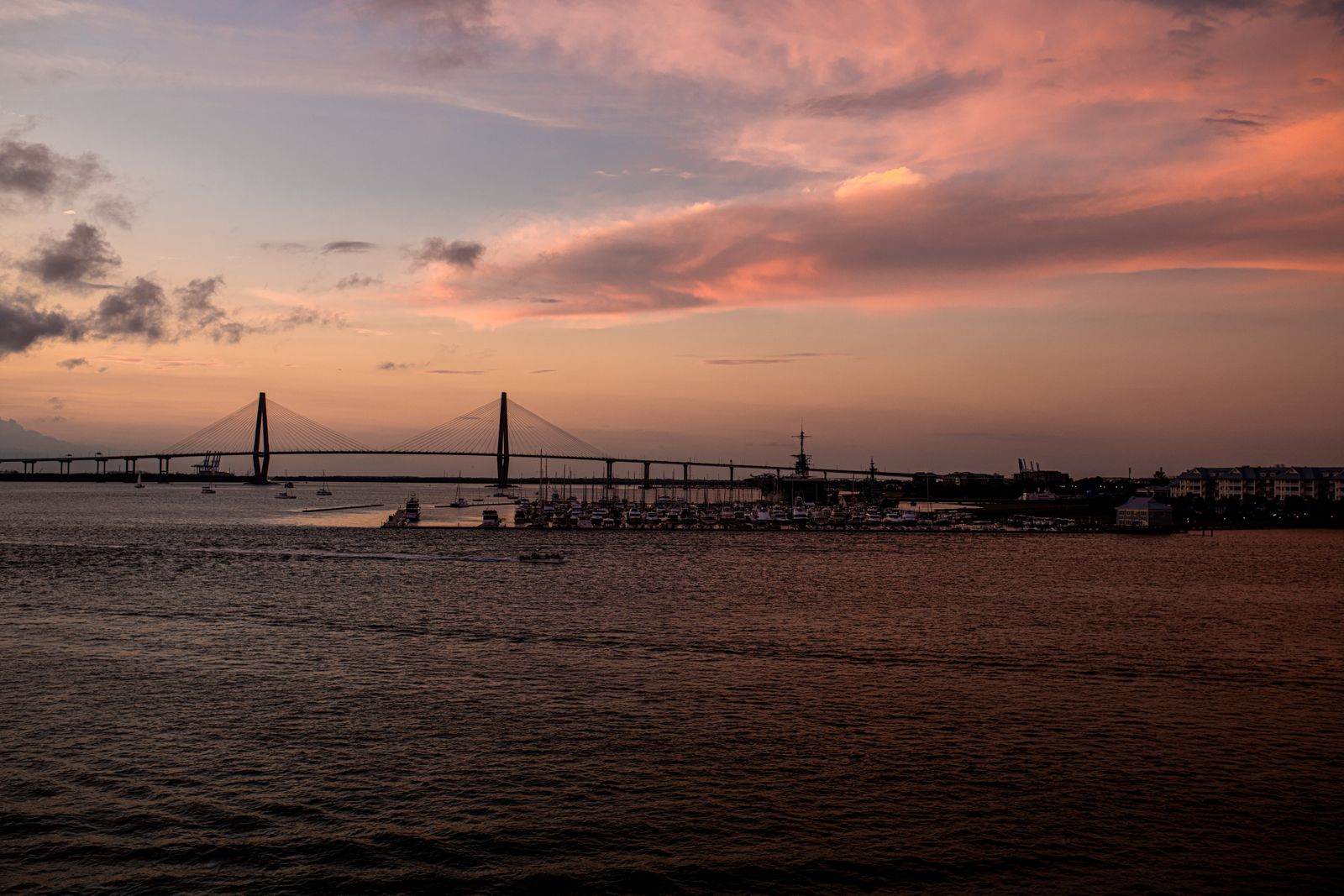 The Ravenel Bridge at sunset from the harbor. The evening cruise and the Shem Creek boardwalk both face this way; pick one.