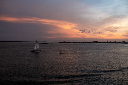 Free A serene sunset over the sea with a lone sailboat creating a peaceful ambiance. Stock Photo