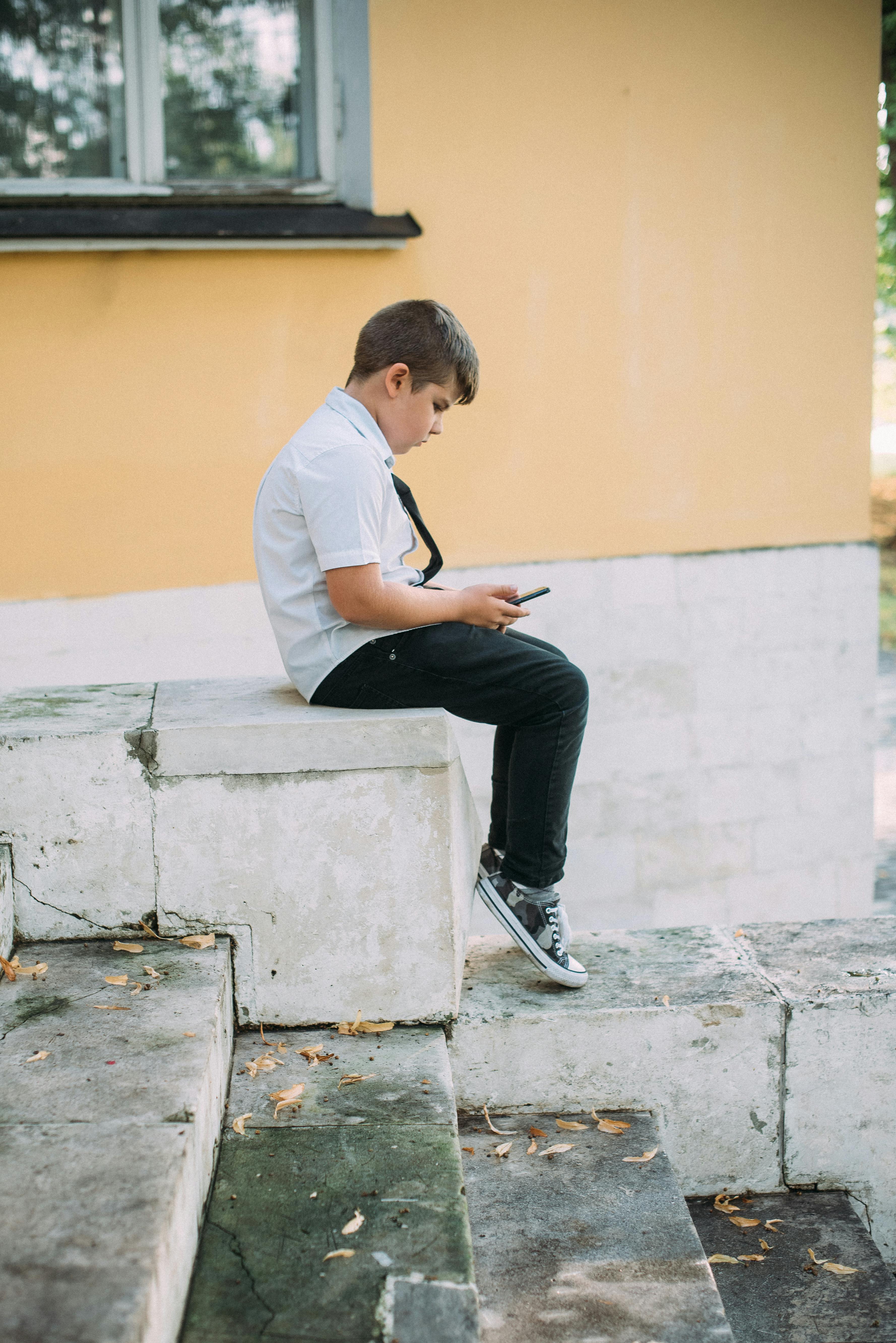 a young boy sitting on a concrete stairs while using his phone