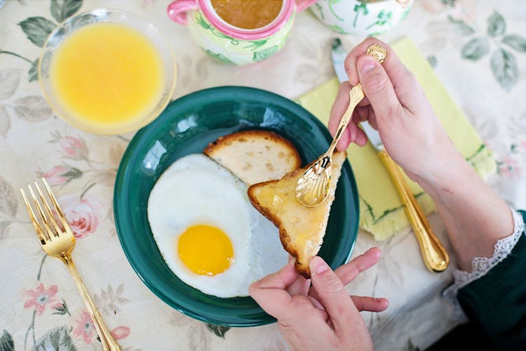 A Person Holding A Toasted Bread And A Gold Teaspoon