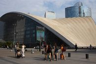 People walking outside a modern architectural building in La Défense district, Paris.