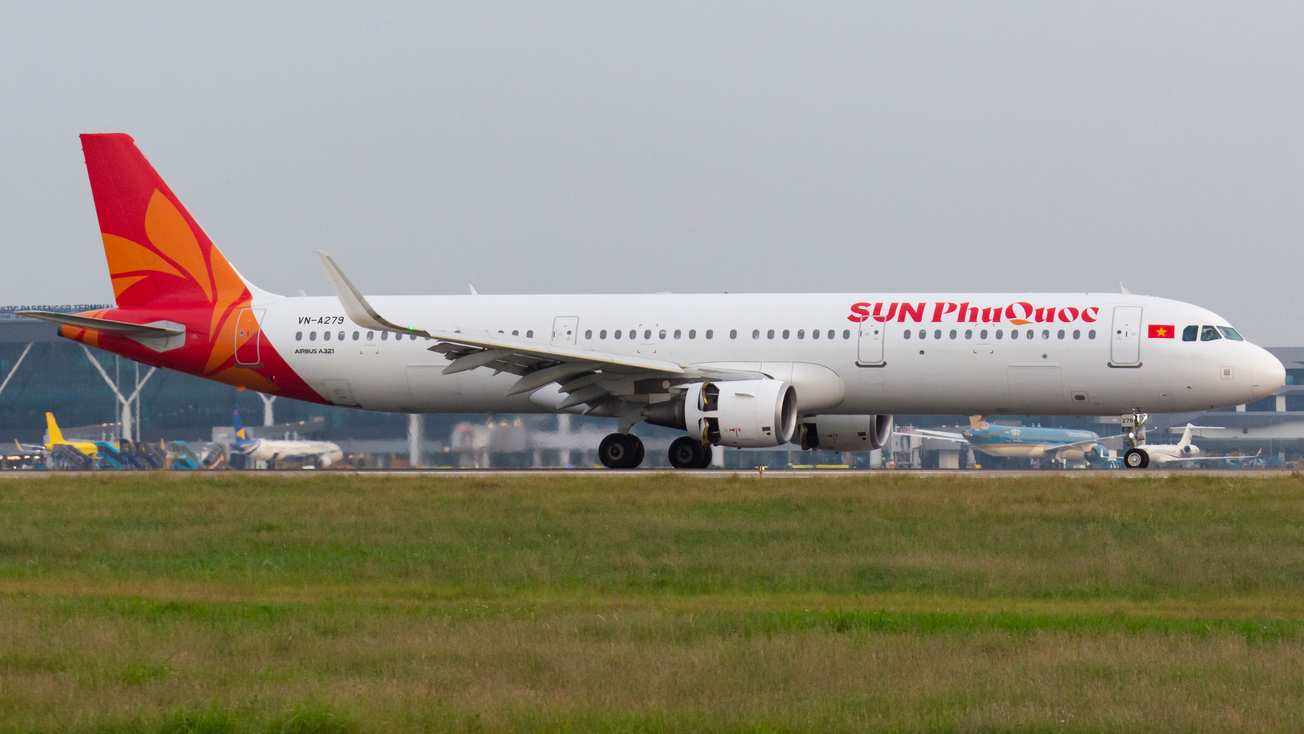 An Airbus A321 branded 'SUN Phu Quoc' on the runway at an airport with visible hangars and other aircraft. — lounges at Phu Quoc Airport