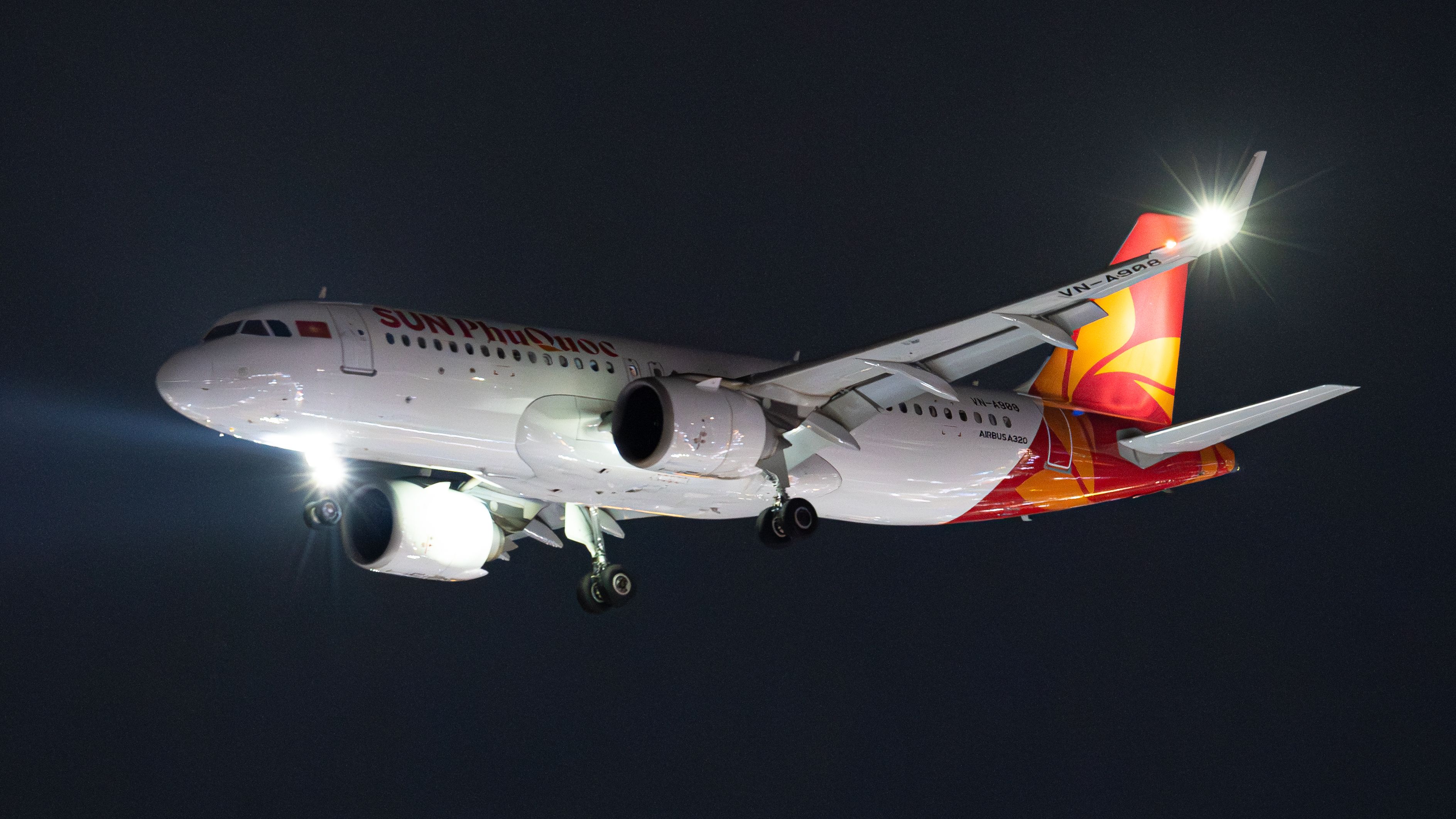 A SunExpress Airbus A320 airplane captured mid-flight with headlights illuminating at night.