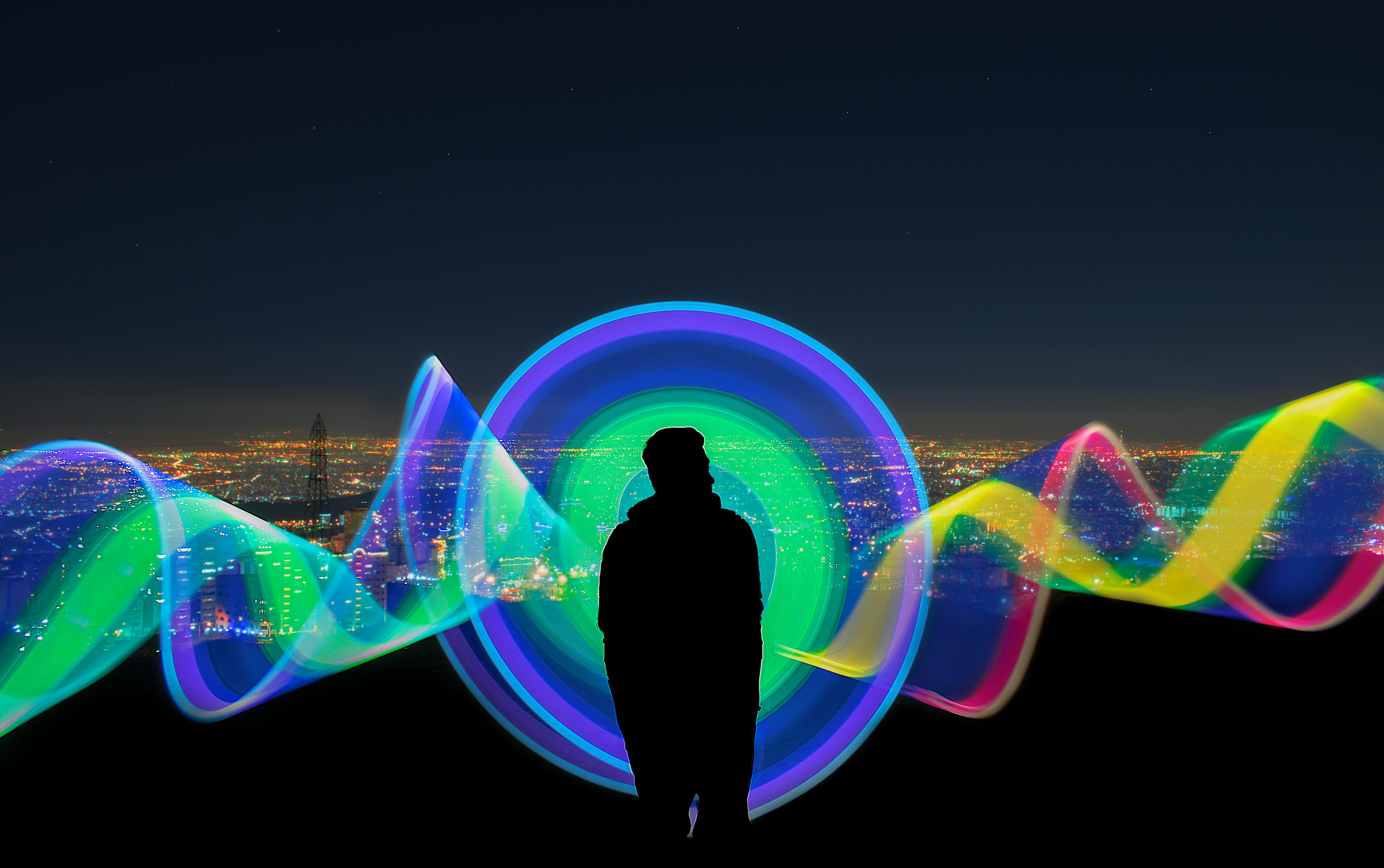 Silhouette of a person against a cityscape with vibrant colored light trails at night.