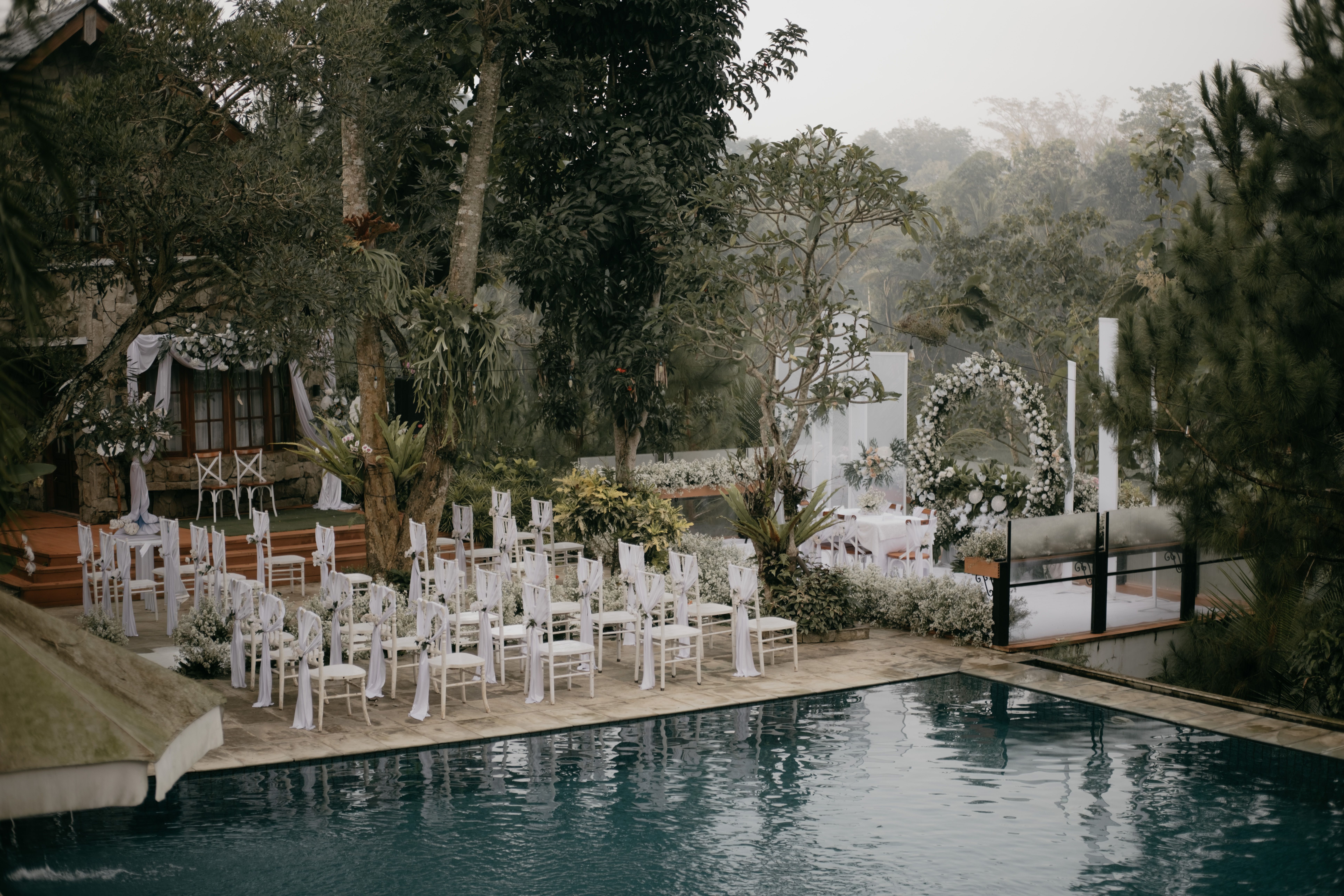 Un lieu de mariage extérieur magnifiquement aménagé au bord d'une piscine, avec une décoration élégante et une verdure luxuriante.
