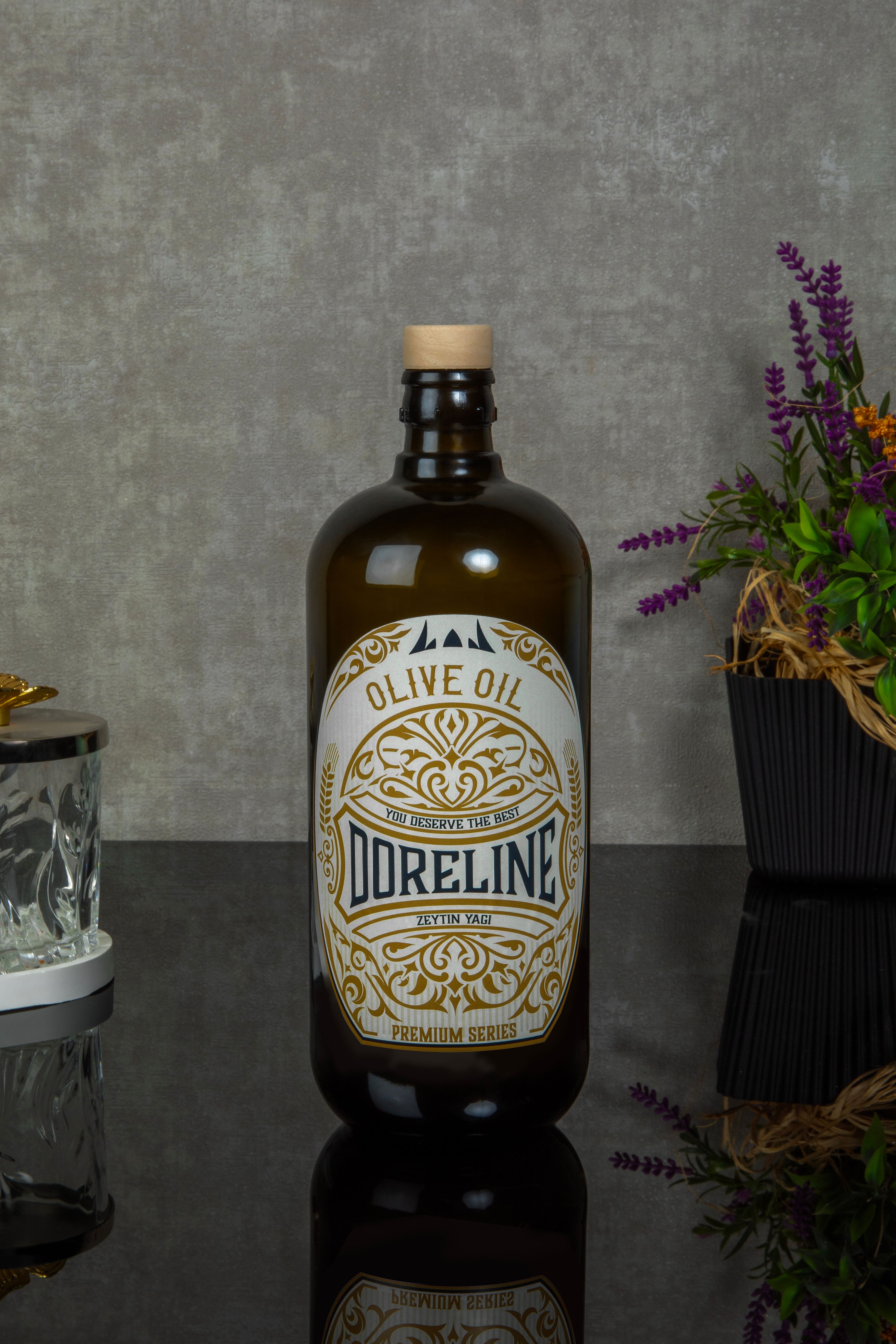 Elegant olive oil bottle with decorative label on a reflective surface with floral accents.