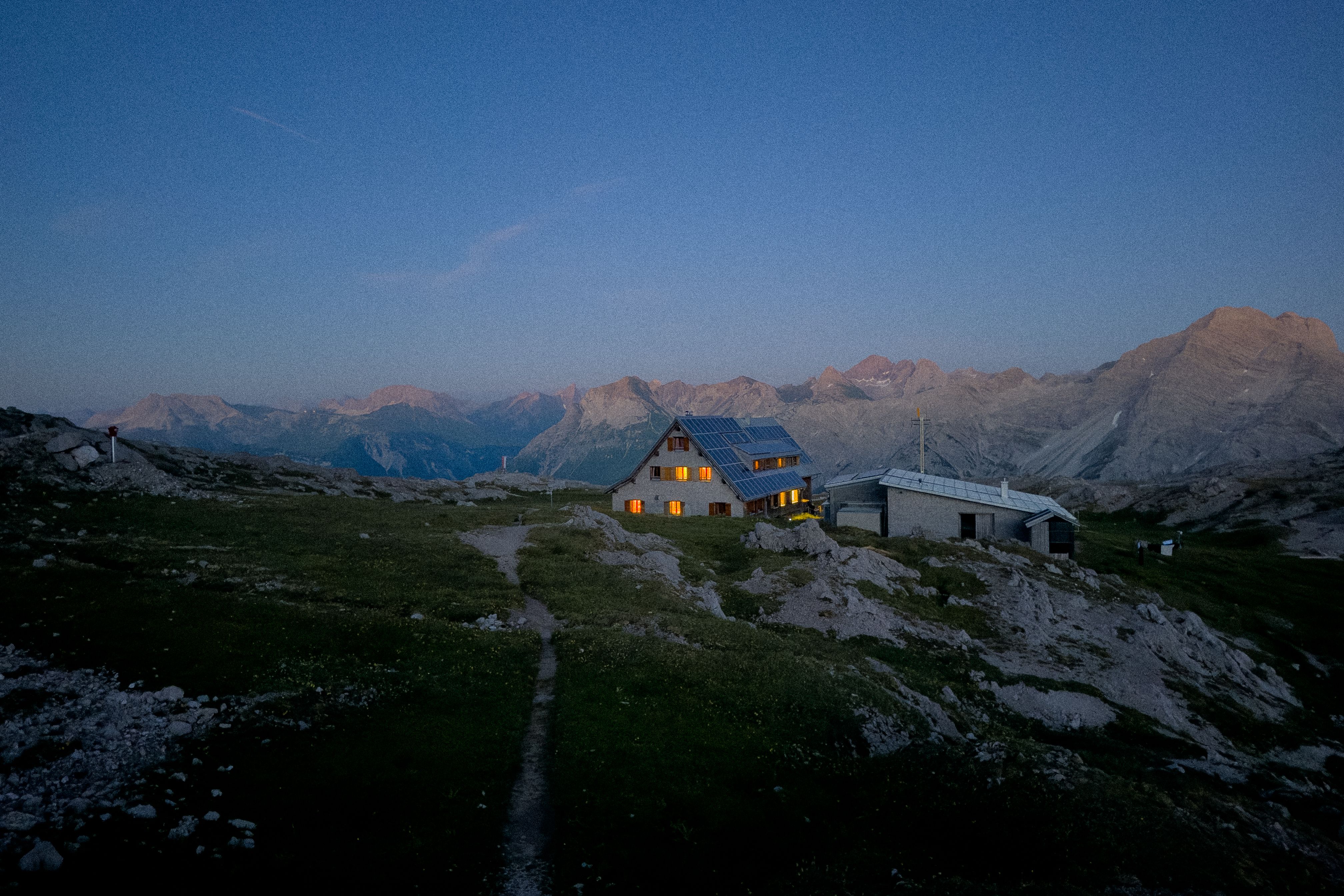 A serene alpine hut in the Austrian mountains at twilight, glowing warmly against rugged peaks.