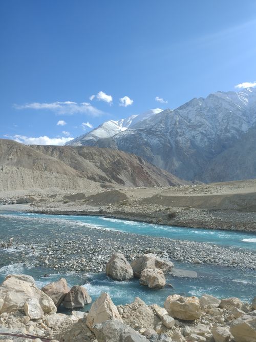 Free A pristine mountain river flowing through a rocky valley with snow-covered peaks under a clear sky. Stock Photo