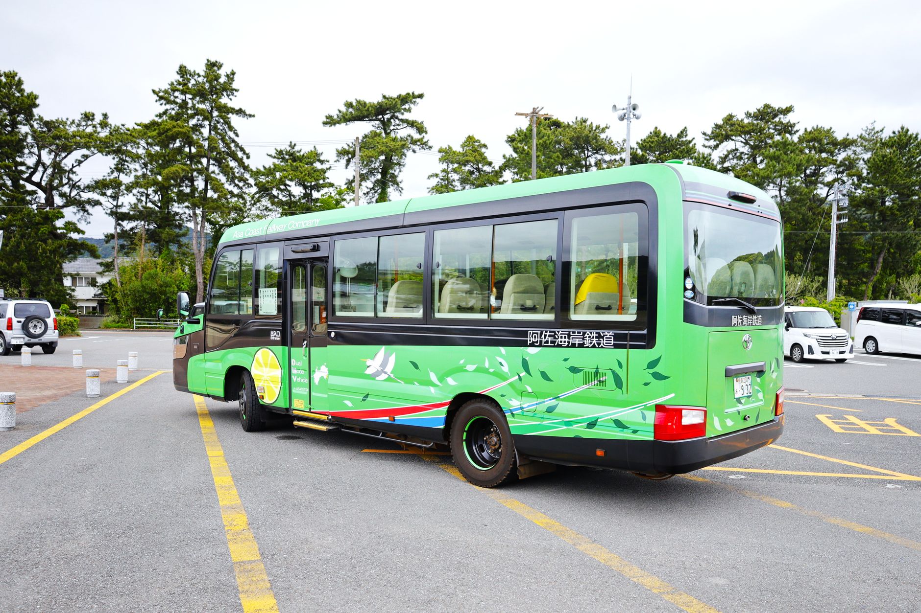 A vibrant dual-mode vehicle parked outdoors in Toyo, Kochi, Japan surrounded by trees.