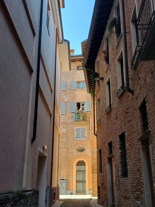 Free A narrow European alley framed by rustic brick walls under a clear blue sky. Stock Photo