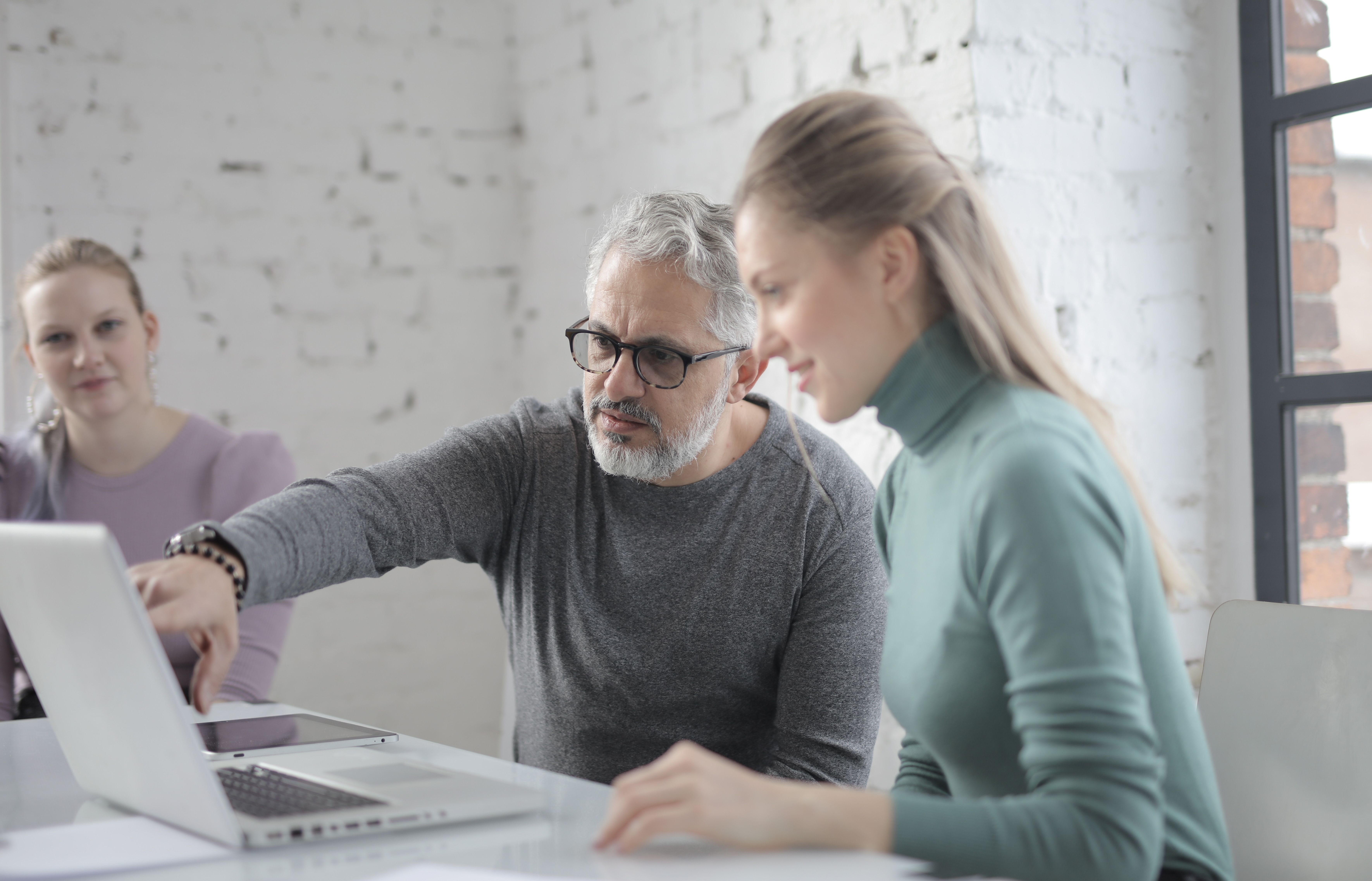 A professional discussing information with a colleague while both look at a laptop screen, representing a referral partner check-in conversation