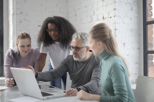 A diverse team of professionals collaborating and discussing a project over a laptop in a modern office.
