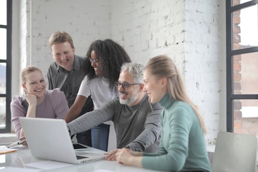 A group of diverse colleagues working together in a modern office setting on a laptop.