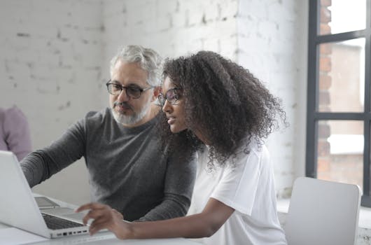 Two colleagues focused on a laptop, collaborating on a project in a modern office setting.