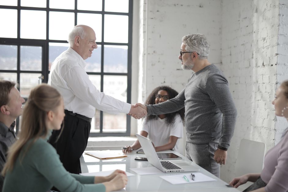Profesionales de negocios dándose la mano durante una reunión de oficina, simbolizando trabajo en equipo y cooperación.