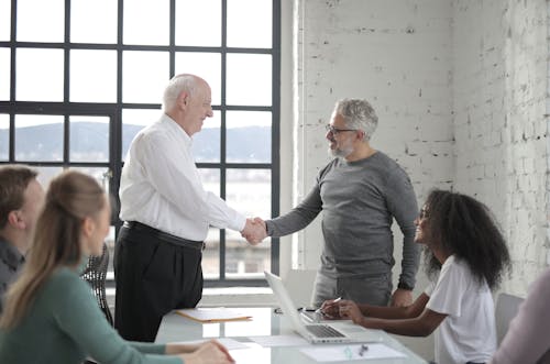 Free Group of diverse coworkers in office man middle aged and man senior shacking hands while working on project with colleagues Stock Photo