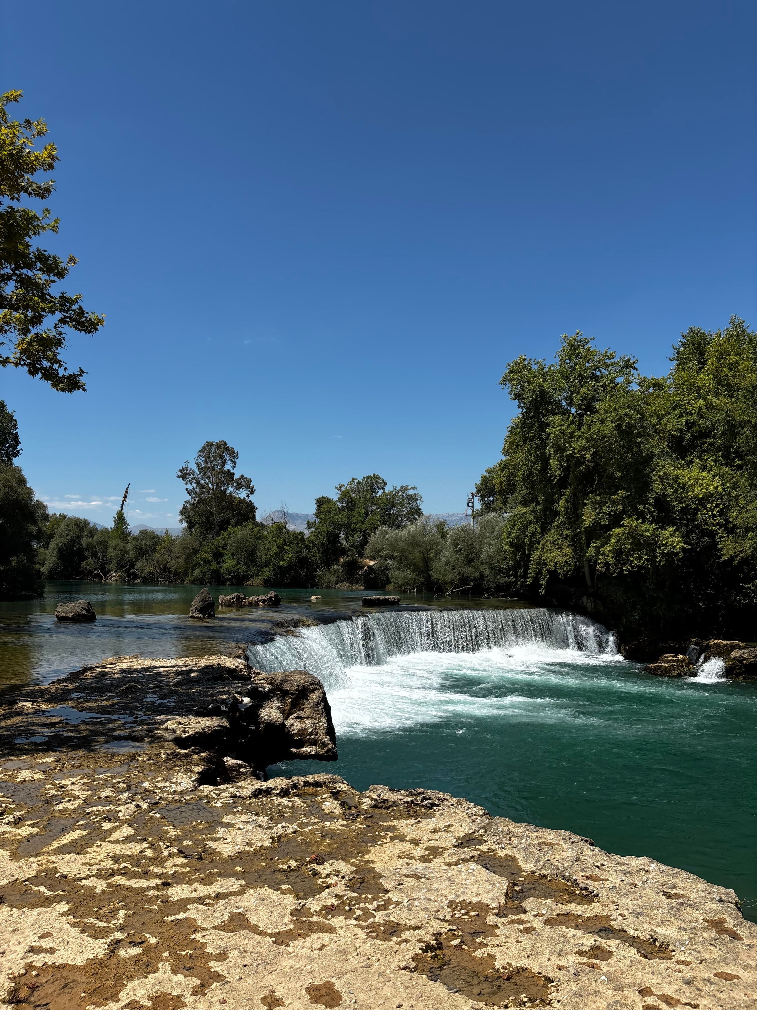 Clear waterfall cascading under a blue sky with lush greenery around.