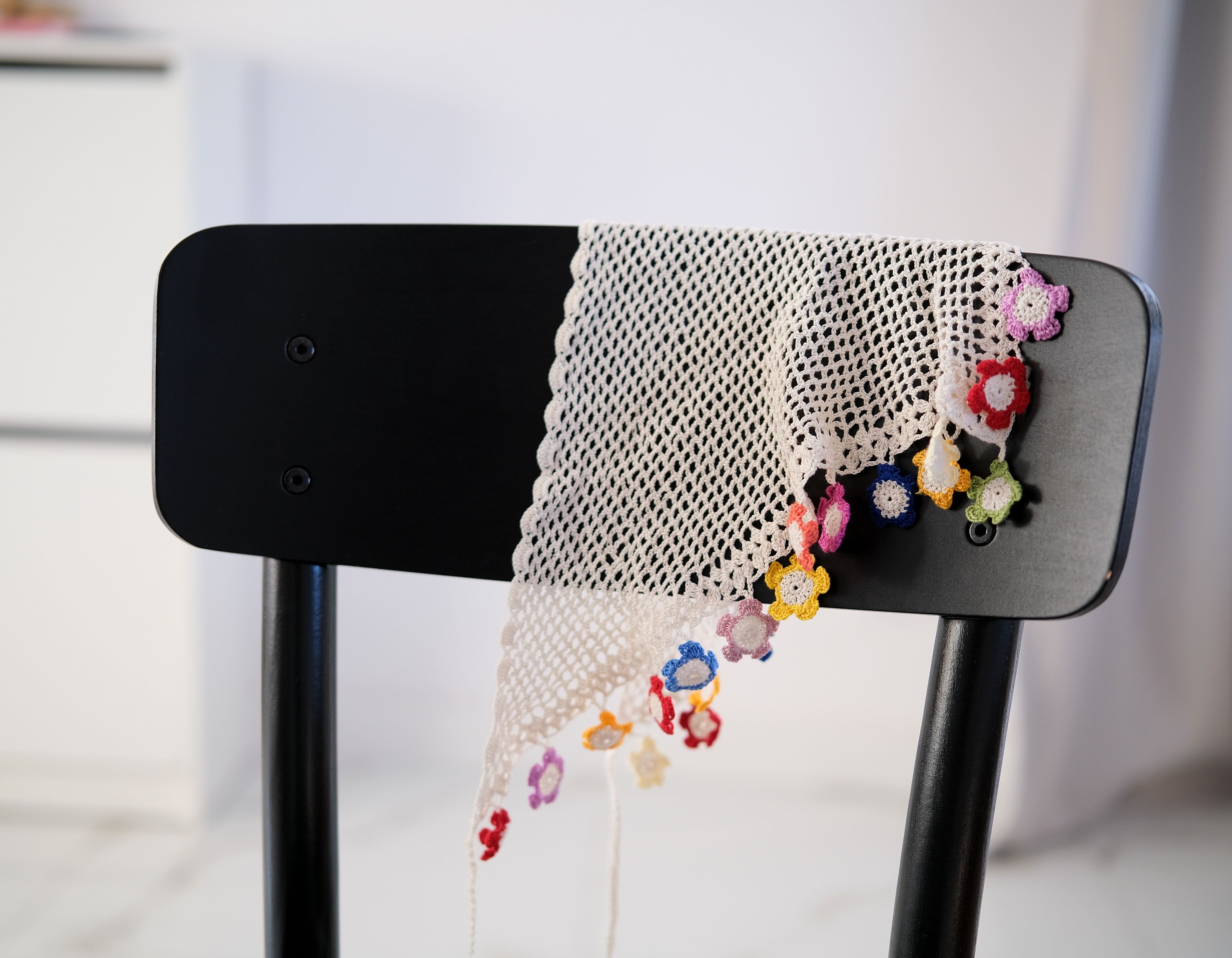 Colorful crocheted fringe with floral patterns draped over a modern black chair indoors.