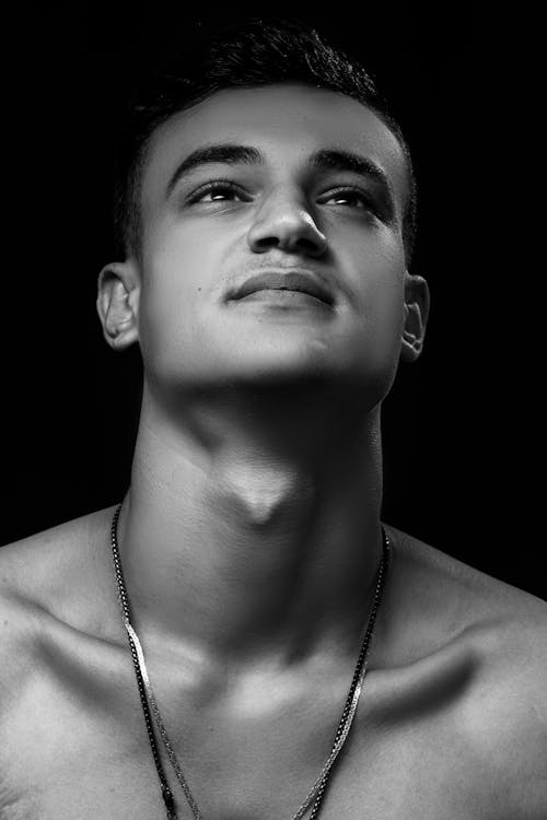 A Grayscale Photo of a Man Wearing Necklace while Looking Up