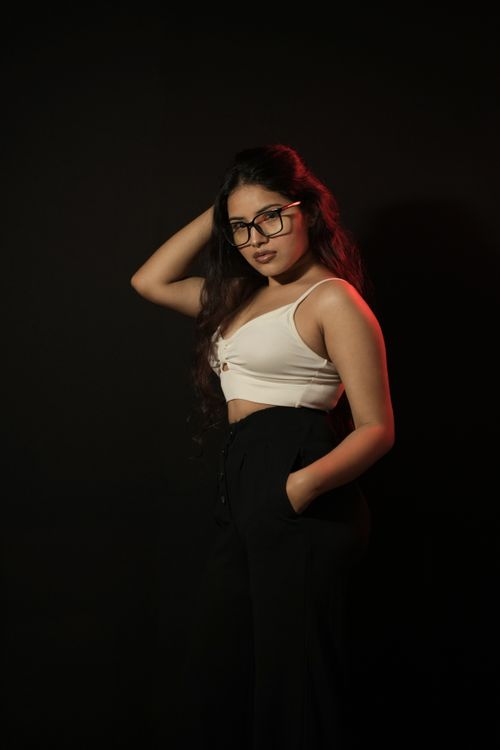 Free Fashionable young woman posing confidently in glasses against a dark, minimalist background. Stock Photo
