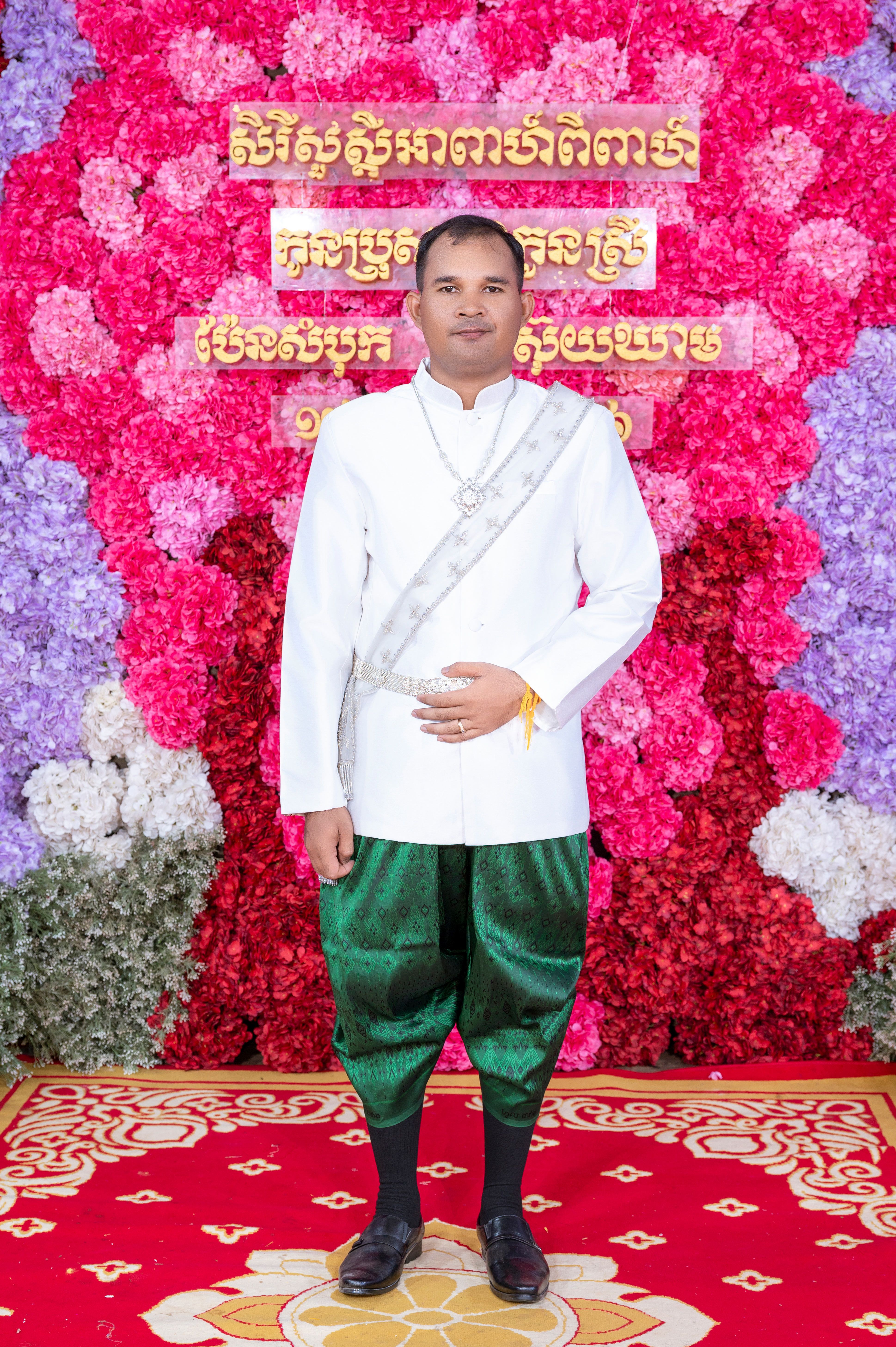 Man in traditional Khmer wedding attire standing against a floral backdrop in Cambodia.