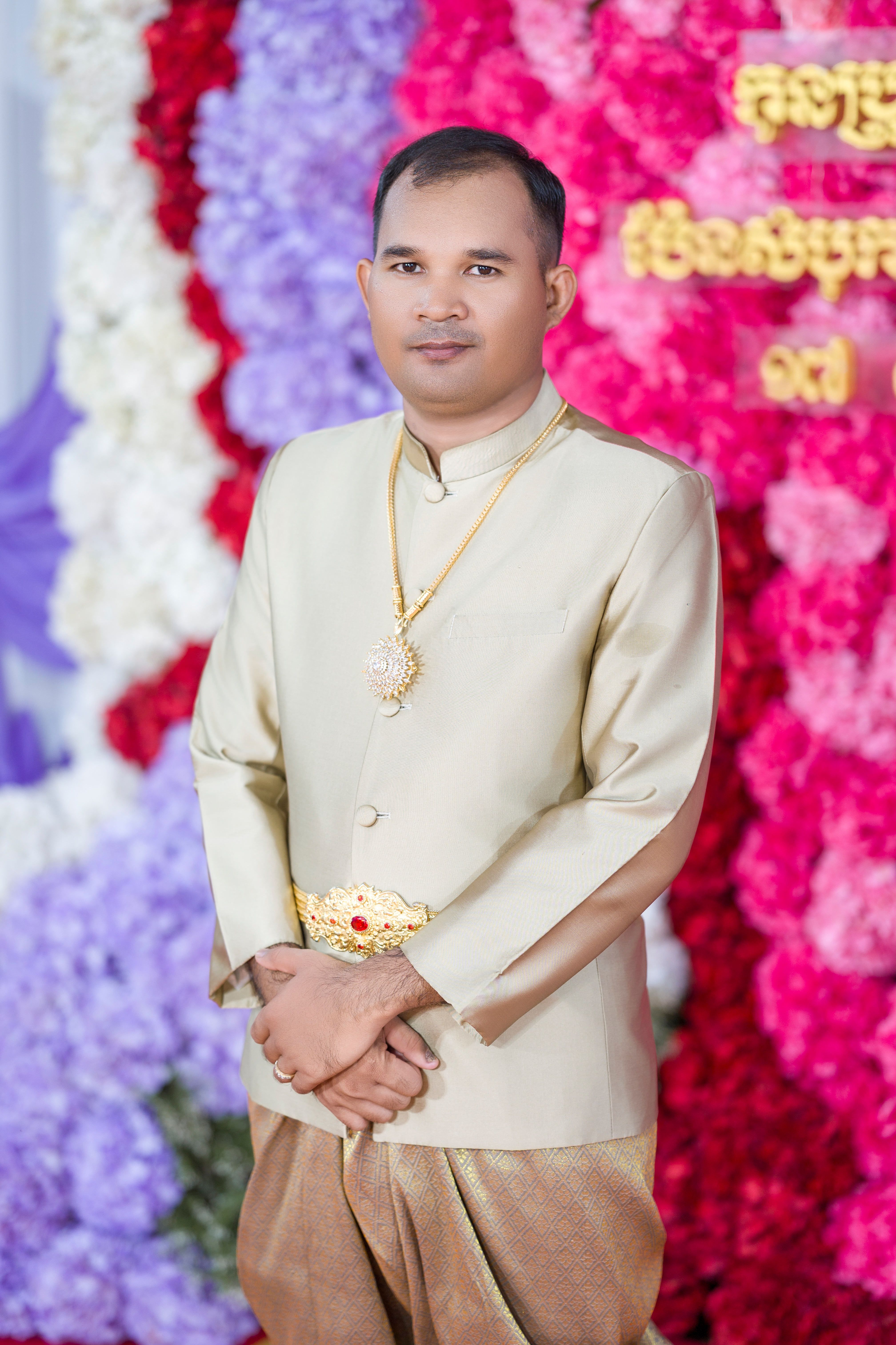 Portrait of a man in traditional Cambodian wedding attire with vibrant floral background.