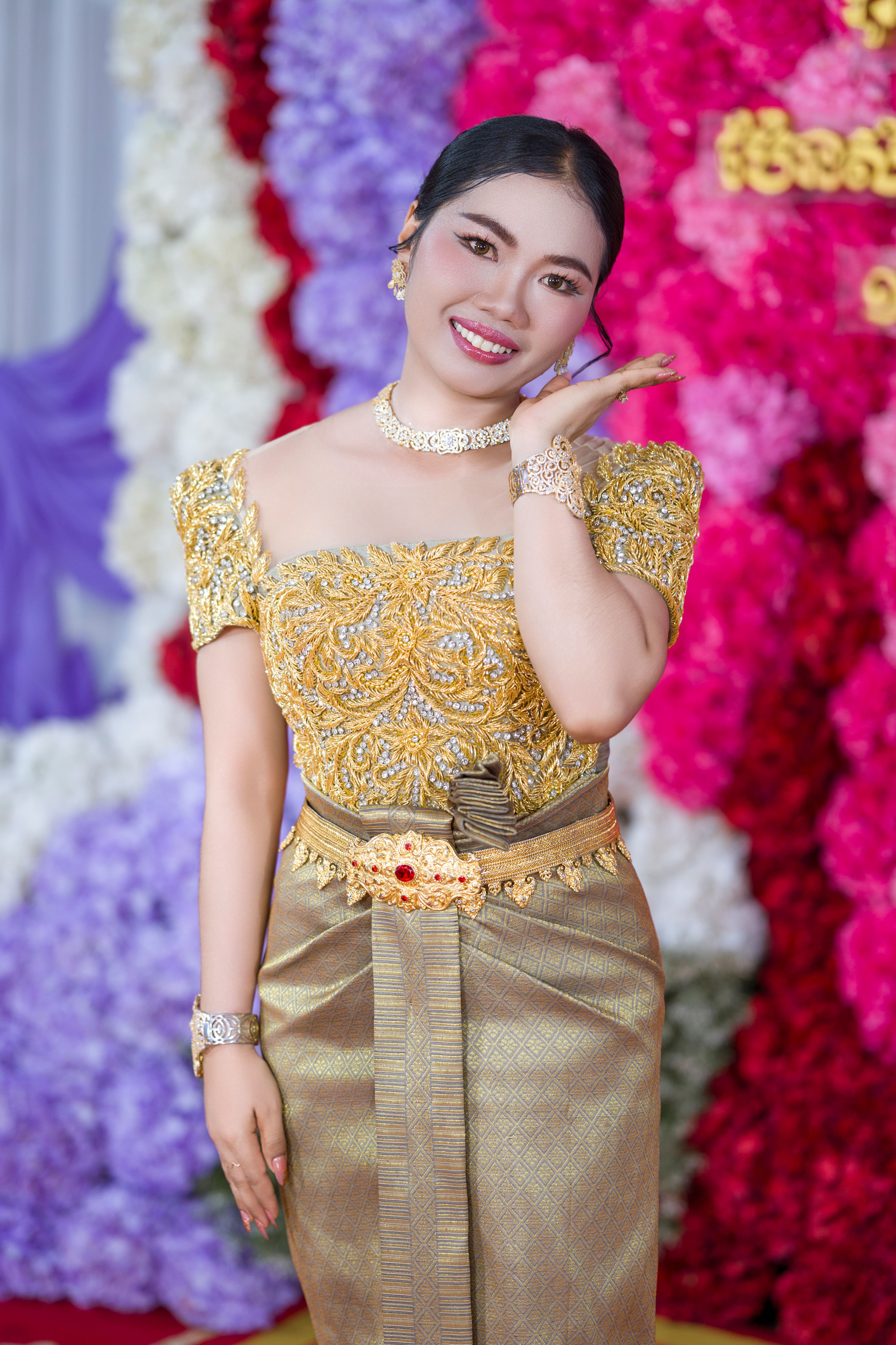 A woman in traditional Khmer wedding attire, surrounded by vibrant floral decorations in Cambodia.
