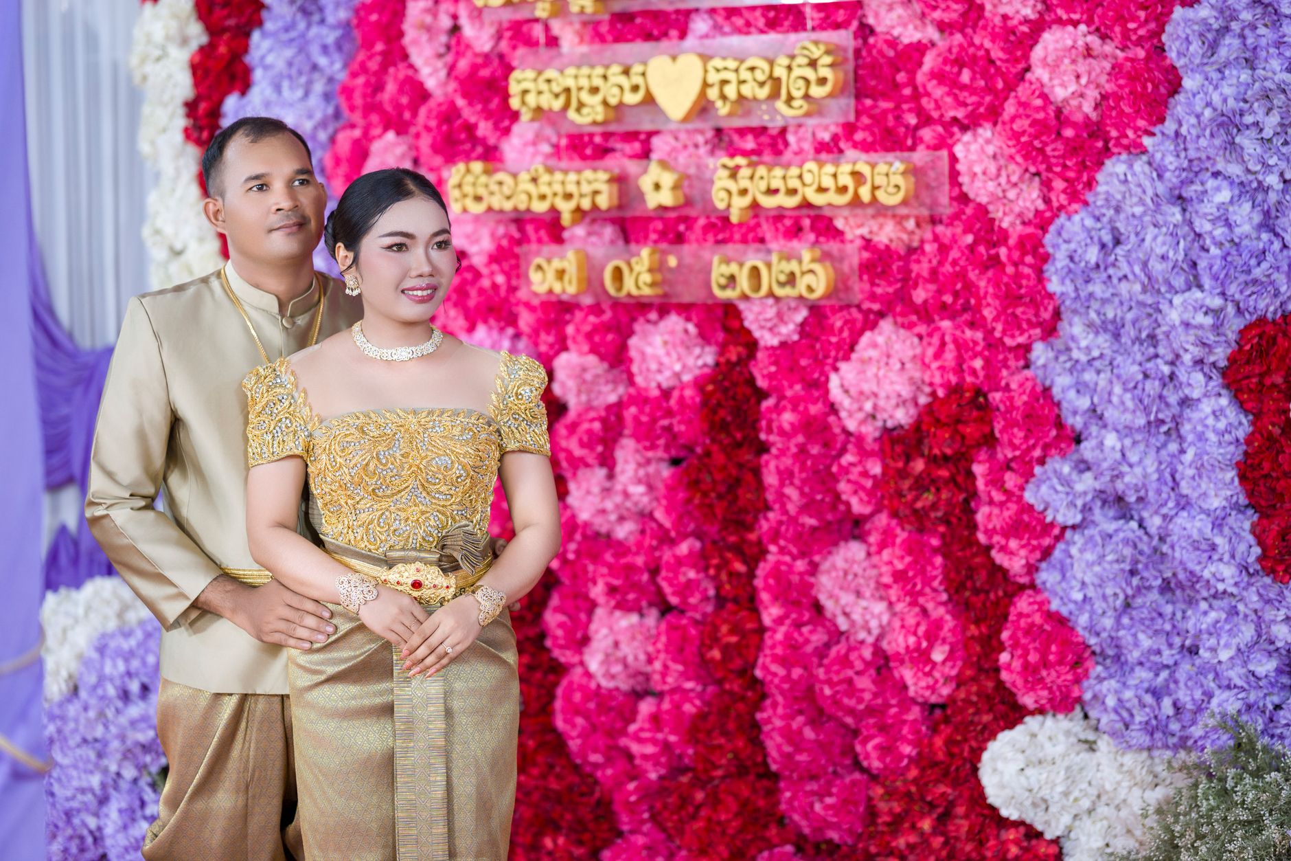 Elegant couple in traditional Cambodian attire at a colorful wedding celebration.